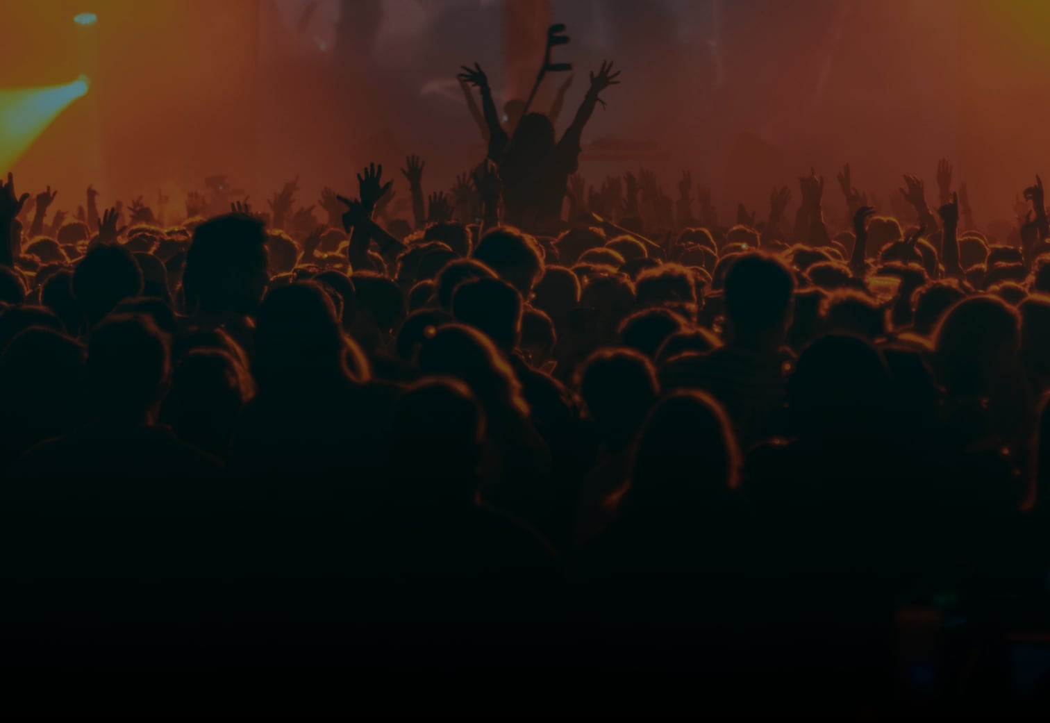 A packed concert crowd with hands raised under stage lights